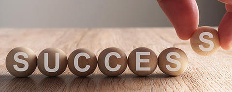 Image of marbles spelling out the word success being placed by someone's hand